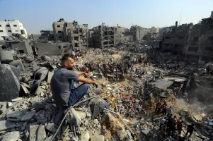 A man sits on the rubble as others wander among debris of buildings that were targeted by Israeli airstrikes in Jabaliya refugee campin northern Gaza Strip